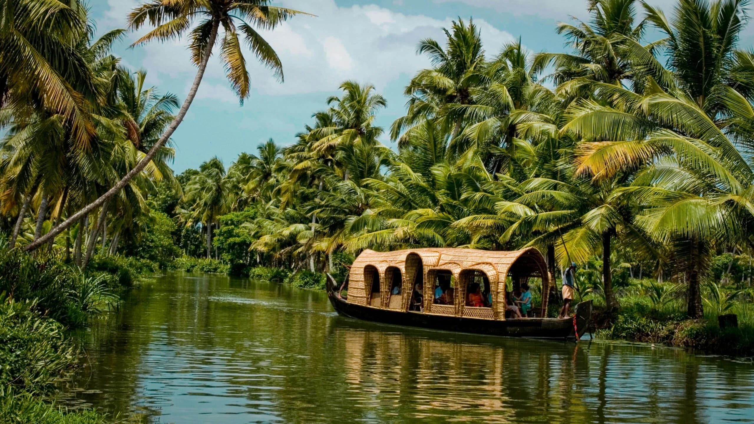 A traditional houseboat gliding through Kerala backwaters beneath coconut palms
