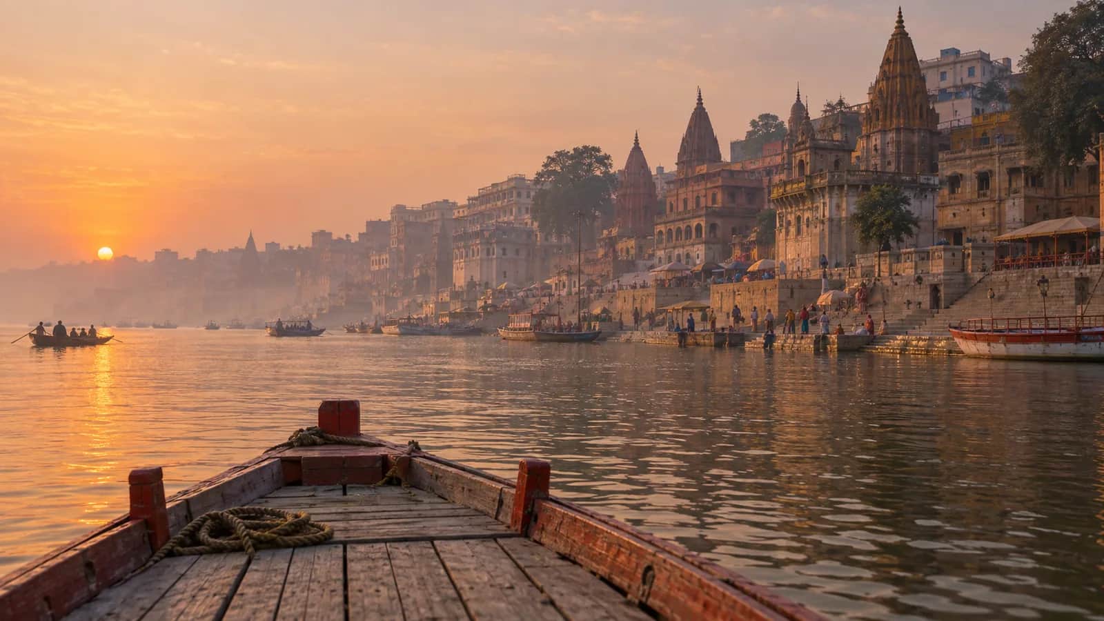 A wooden boat approaching the historic Varanasi ghats on the Ganges at sunrise