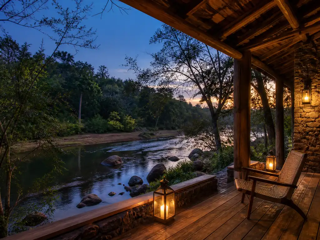 A lantern-lit riverside lodge surrounded by a forested Indian landscape